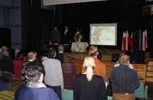 Uroczystość w MDK w Przedborzu - zebrani śpiewają Mazurka Dąbrowskiego; na scenie, za stolikiem, od lewej: wiceprezes TMP i radny w Przedborzu Paweł Zięba, inicjator uroczystości i prelegent Adam W. Gorycki z Kielc. 